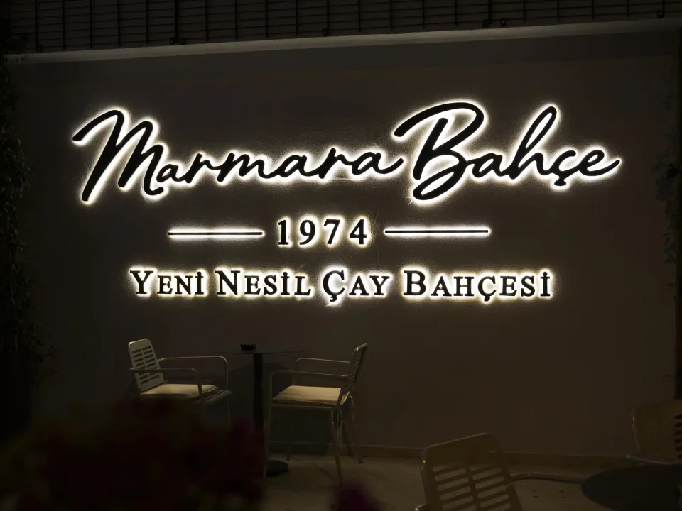 Gece duvarda ışıklı Marmara Bahçe 1974 Yeni Nesil Çay Bahçesi yazısı, altında masa ve sandalyeler
