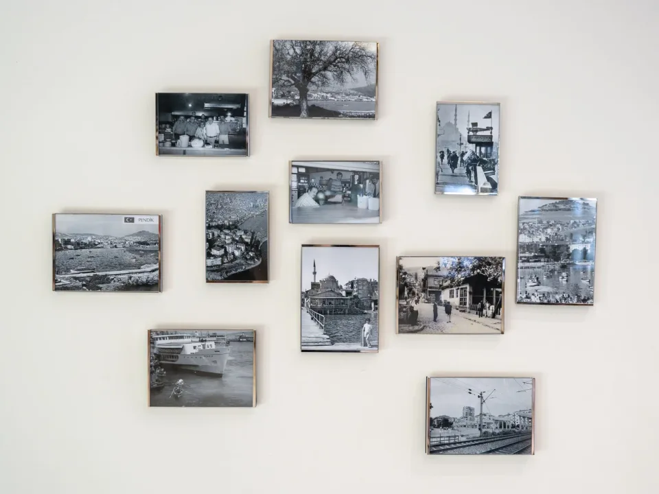Beyaz duvarda, biri PENDİK etiketli, çerçeveli siyah beyaz eski fotoğraflar