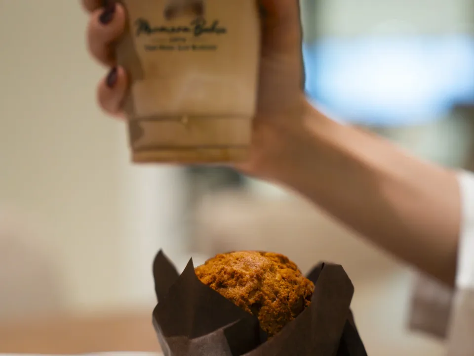 Marmara Bahçe logolu kapta kahveli içeceği tutan el ve önünde kâğıt kalıpta muffin