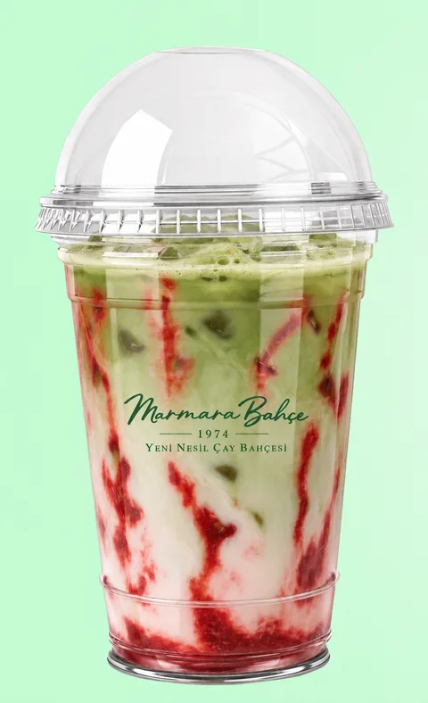 Kubbe kapaklı şeffaf bardakta buzlu matcha latte; yeşil matcha, süt ve çilek sosu katmanları.